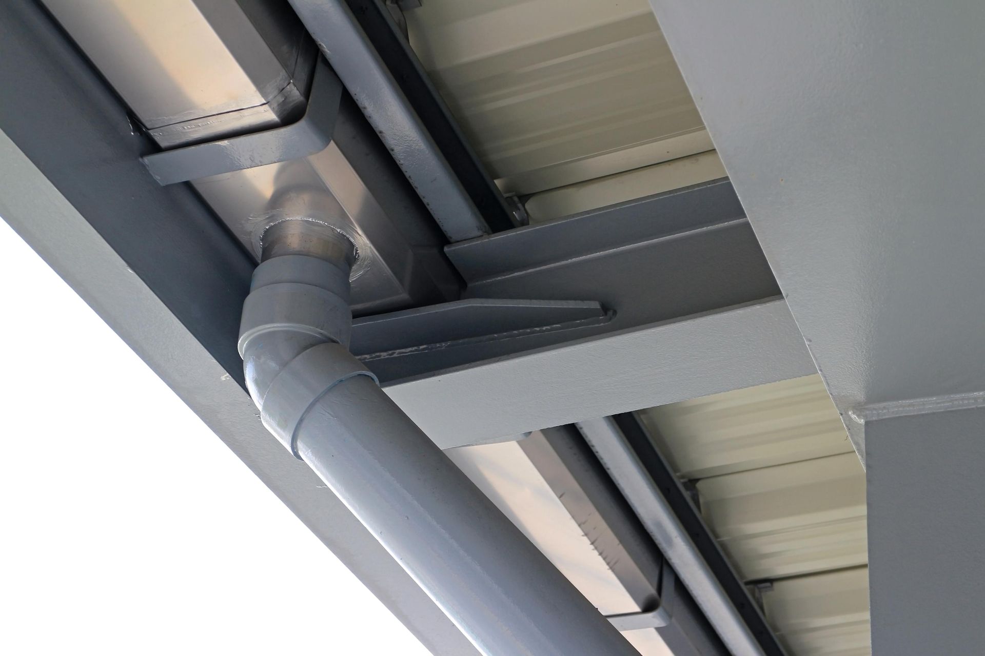 A metal gutter system with a grey downspout attached to the underside of a roof structure.
