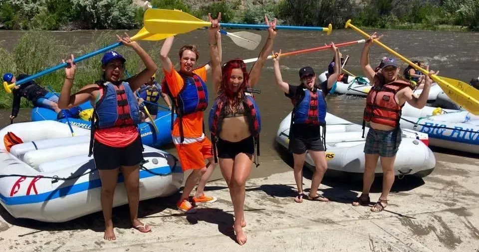 A group of people standing in front of rafts holding oars in the air