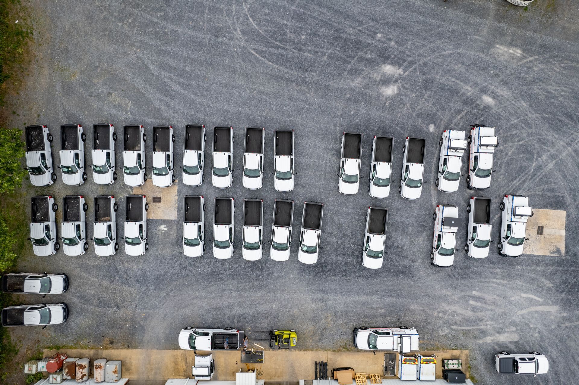 Aerial view of white pickup trucks parked on a gravel lot.
