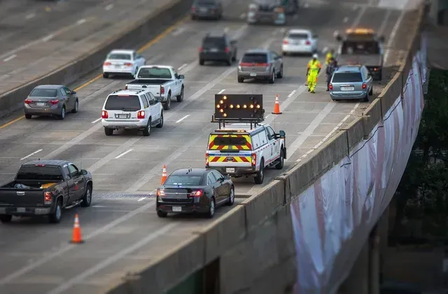Highway traffic with construction vehicle displaying directional arrow.