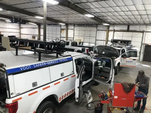 VDOT Safety Service Patrol trucks parked inside a garage. A person works on equipment near an open door.
