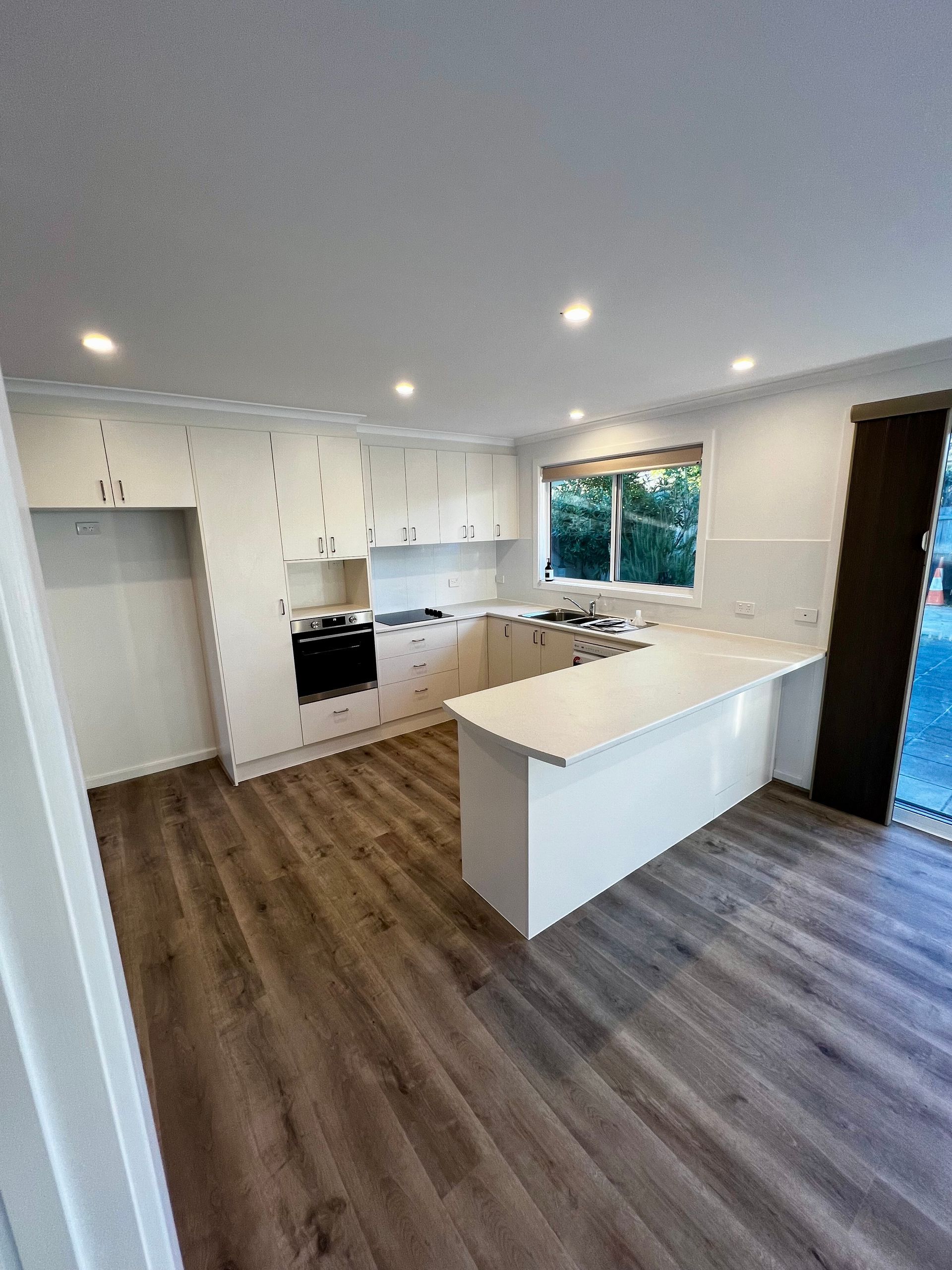 A White Kitchen With Wooden Floors — P & M Maintenance Building Services in Yass River, NSW
