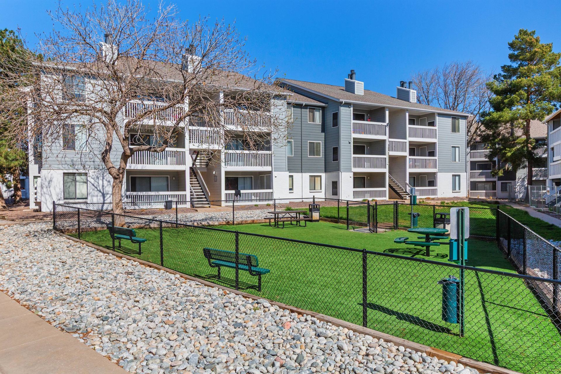 Exterior view of a multi-building apartment complex with a fenced green courtyard and benches.