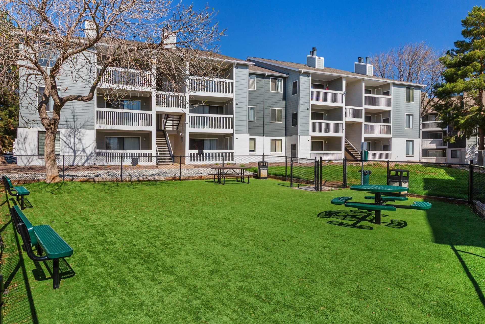 Communal outdoor courtyard with green lawn, benches, and a picnic table in front of apartment buildings.