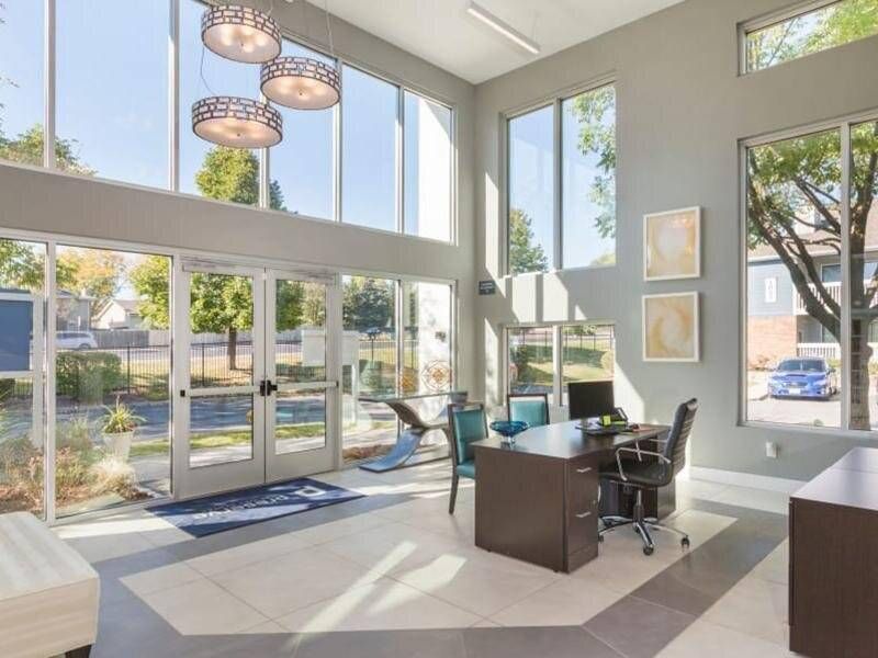 Sunlit leasing office lobby with glass doors, large windows, and a desk.