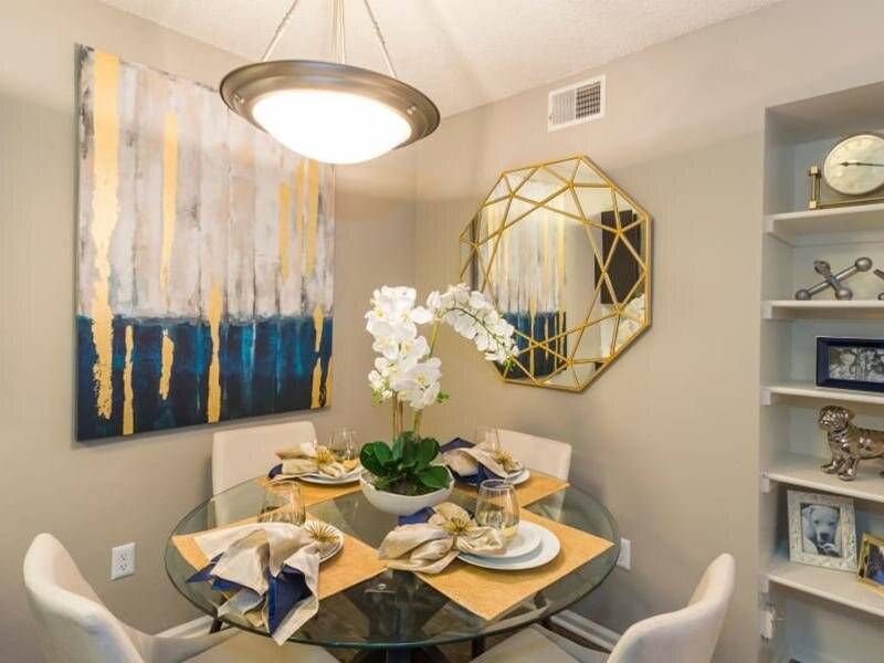 Preserve at City Center dining nook with a round glass table, white chairs, abstract art, and a gold geometric mirror.