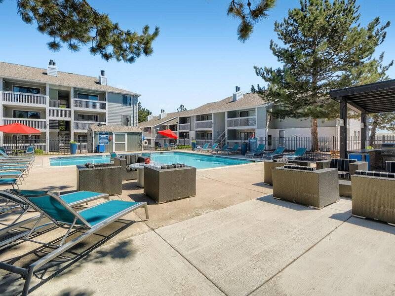 Outdoor apartment community pool with lounge chairs, umbrellas, and surrounding buildings.