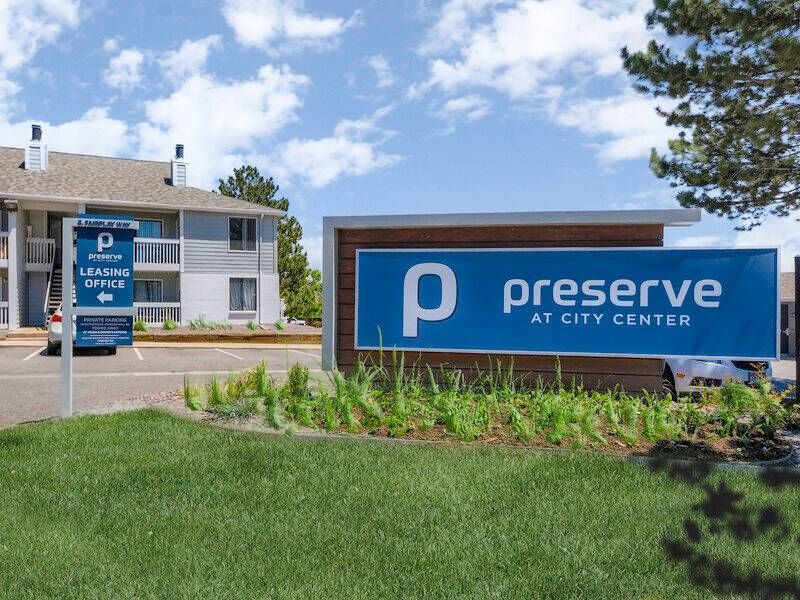 Exterior view of a multifamily community with a blue 'Preserve at City Center' sign and leasing office sign.