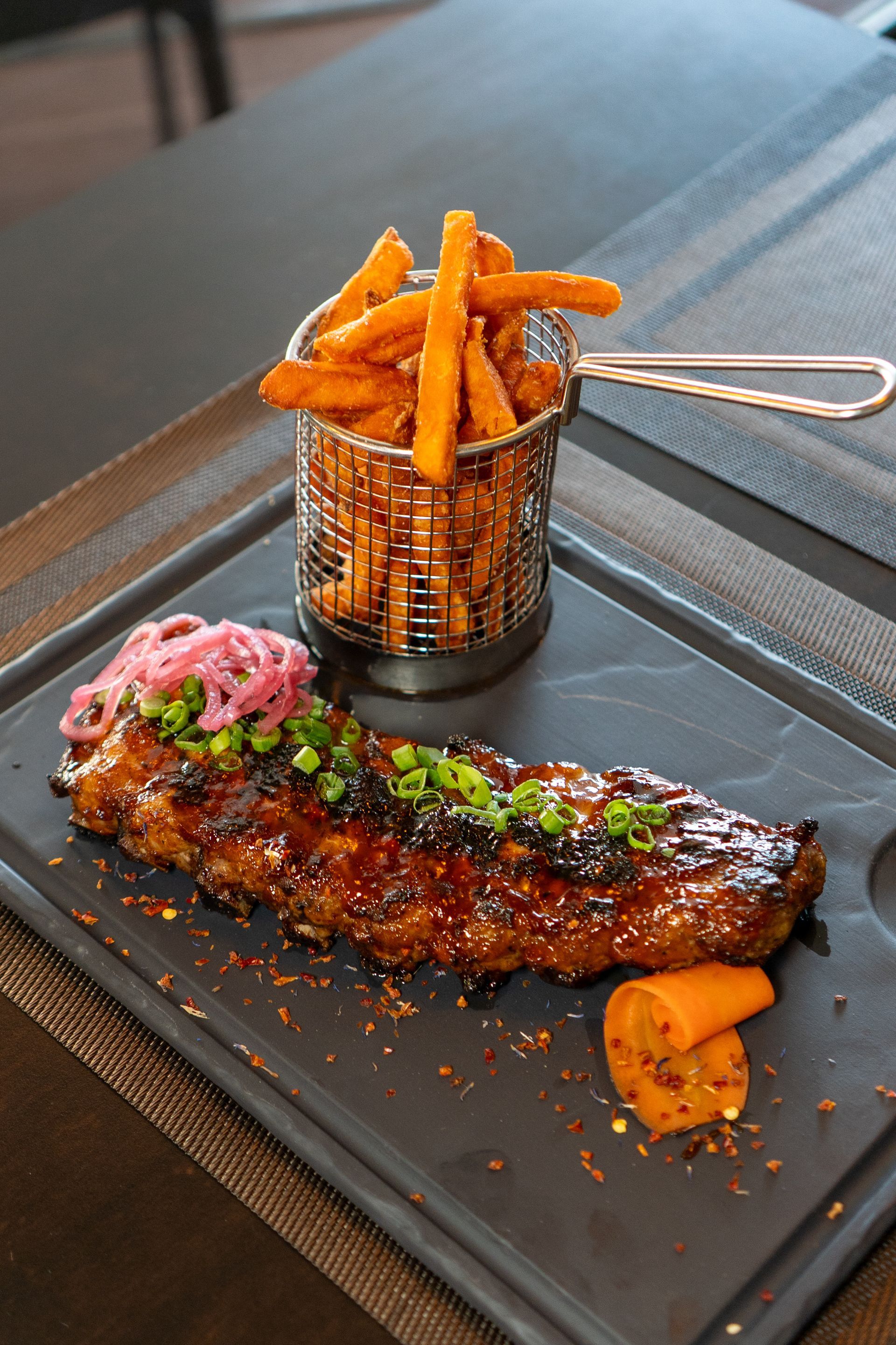 Côtes grillées avec frites de patates douces et oignons marinés sur un plateau sombre.