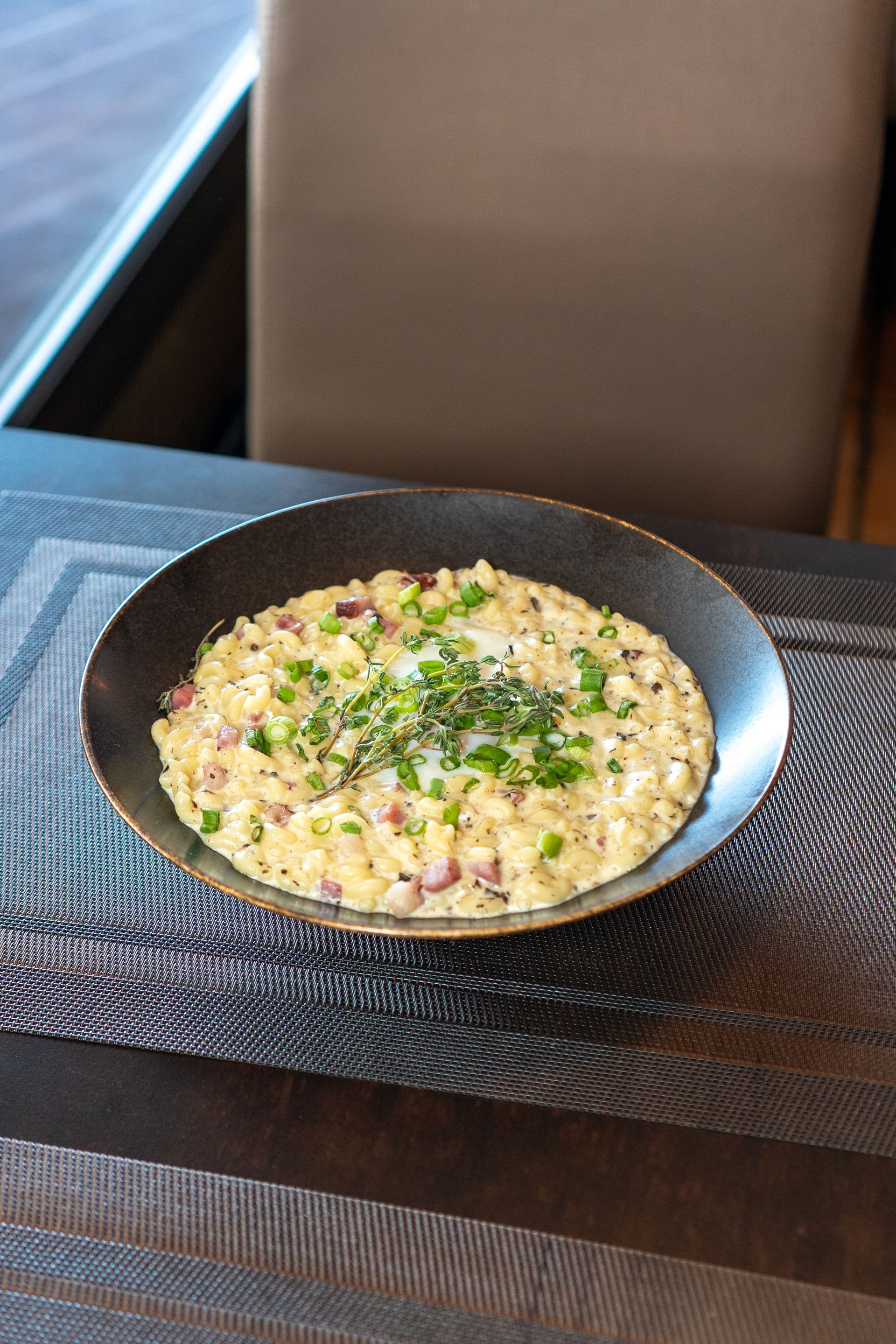 Risotto à la ciboulette dans un bol foncé, sur un set de table texturé, dans un décor de restaurant.