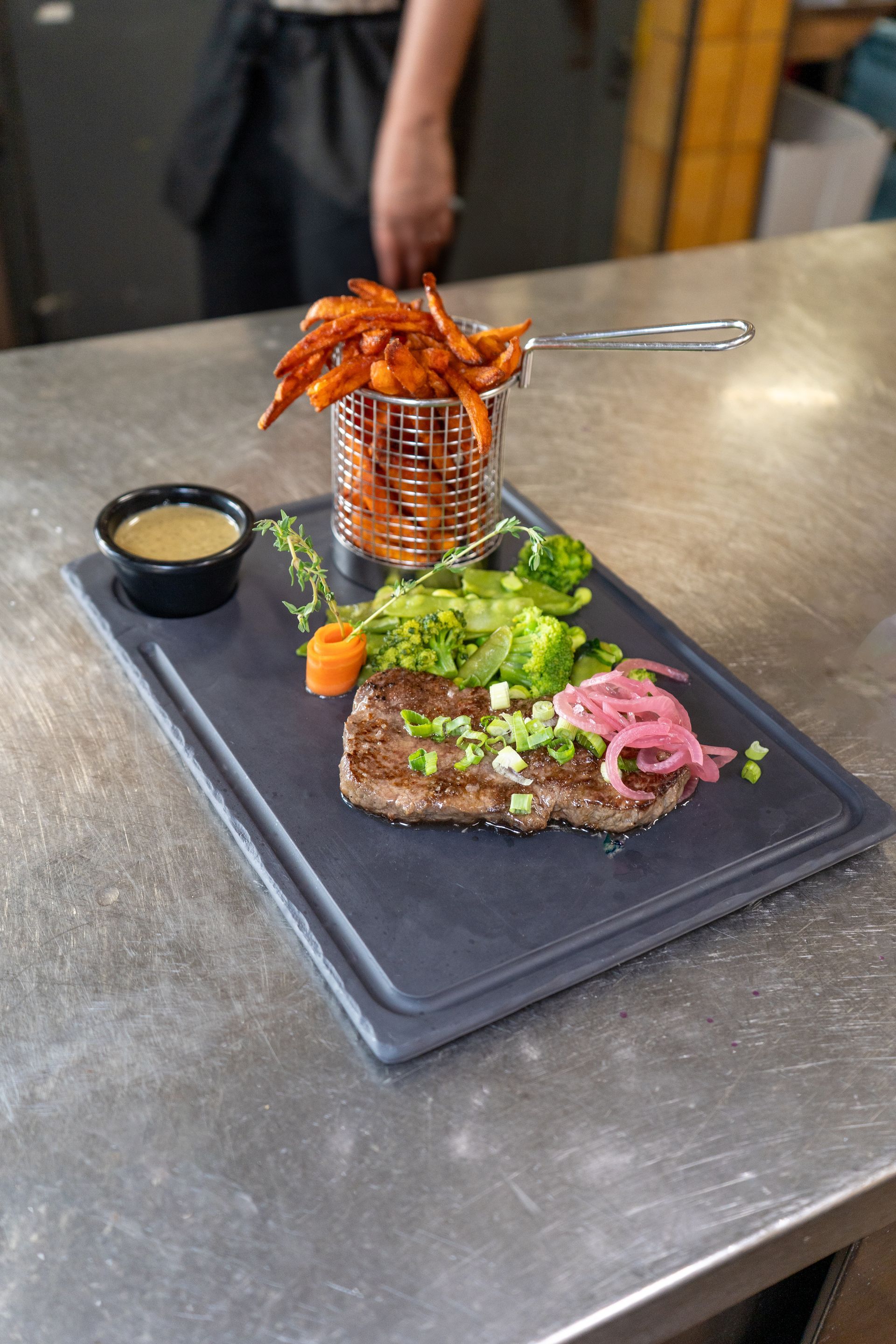 Dîner de steak sur une assiette en ardoise grise avec frites, sauce et légumes.