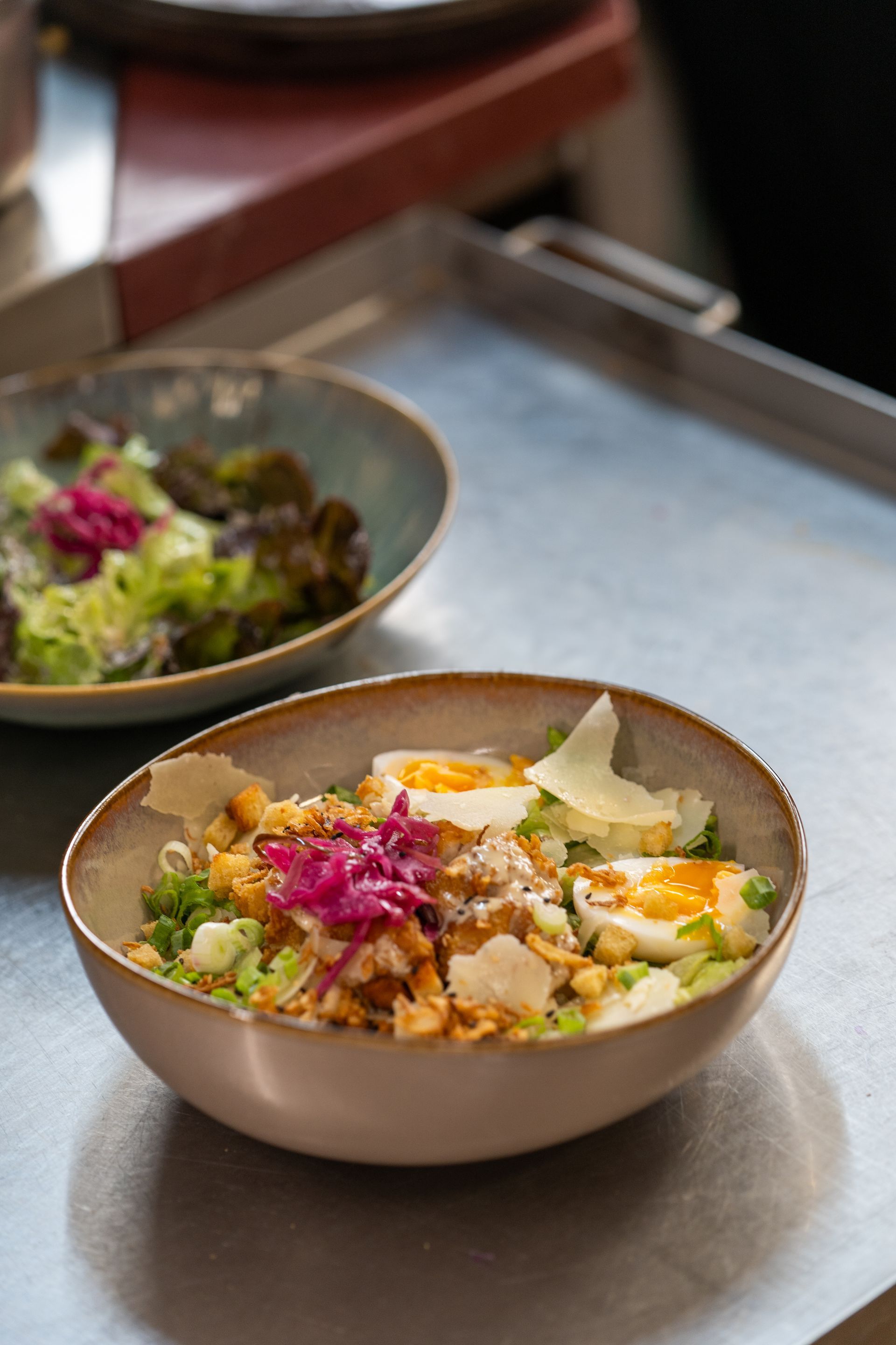 Saladier avec œufs, noix et oignons rouges sur une surface grise ; une autre salade en arrière-plan.