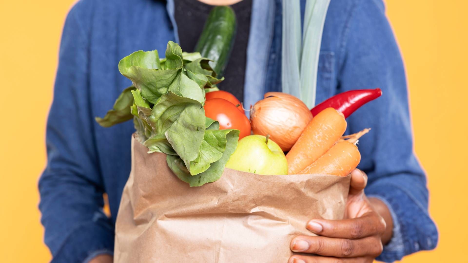 A person is holding a paper bag filled with fruits and vegetables.