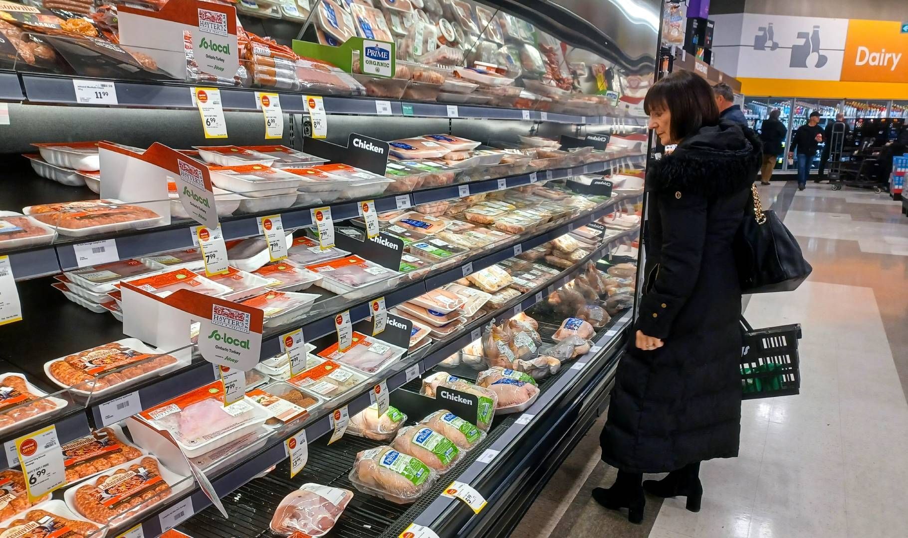 A woman is looking at chicken in a grocery store.