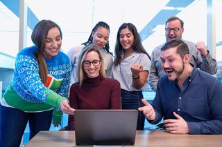 Group of people excitedly looking at a laptop screen in an office. They show expressions of joy and excitement.