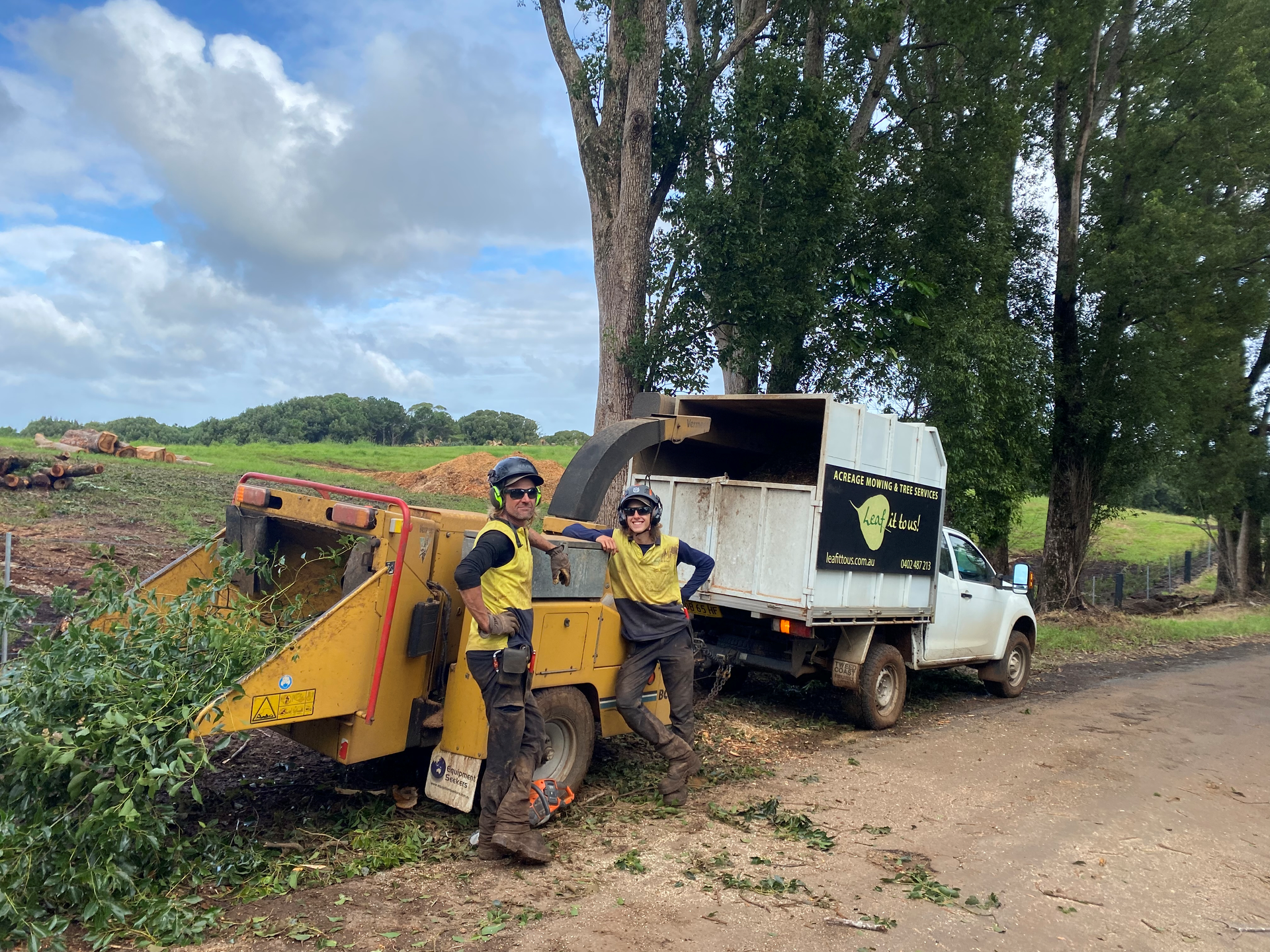 Two People in Work Gear Pose by A Wood Chipper and Truck on A Tree-Lined Road — AAA Trees On Tweed in Ballina, NSW