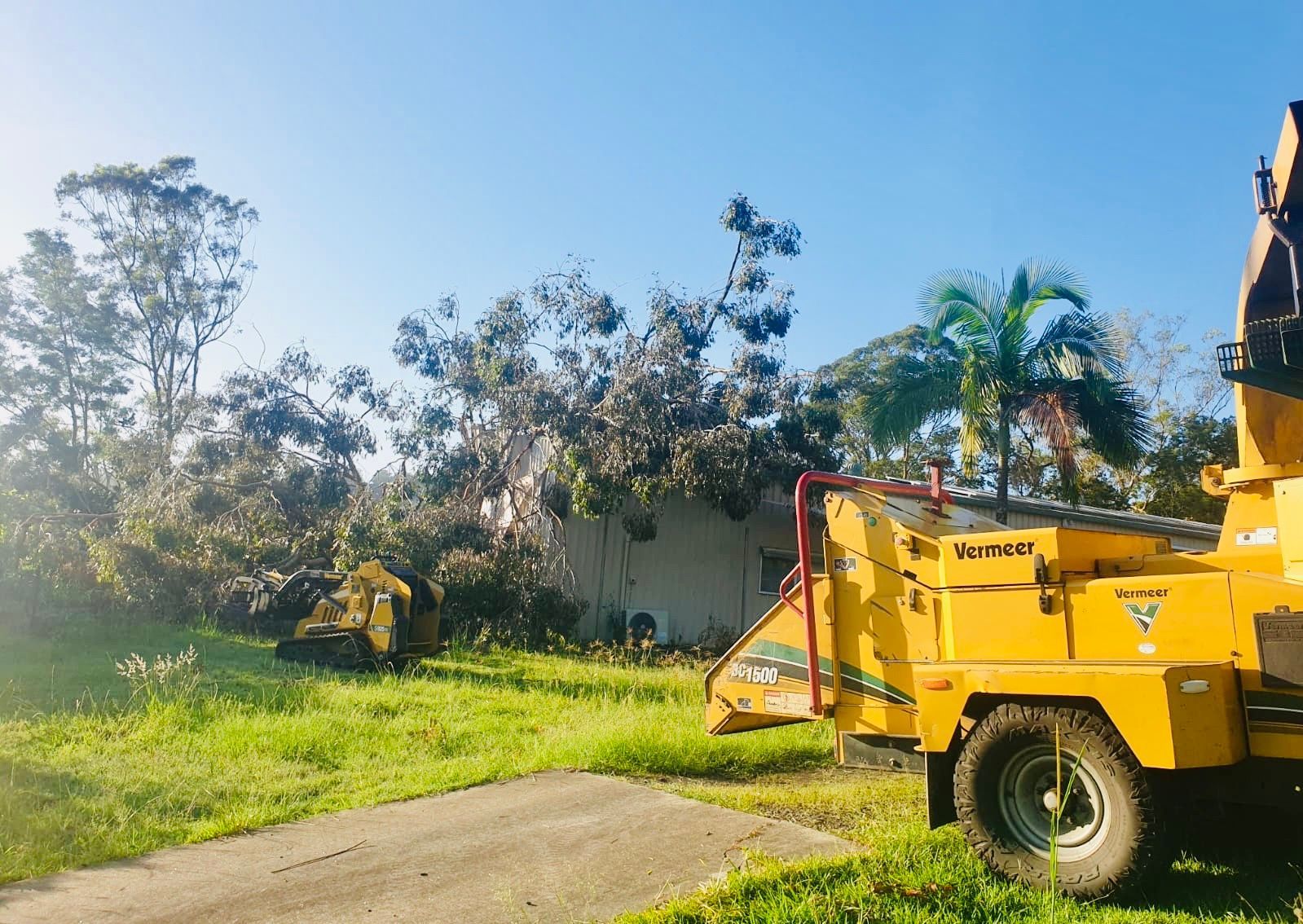 Yellow Wood Chipper on A Sunny Lawn Near a Building with Tree Debris — AAA Trees On Tweed in Clunes, NSW