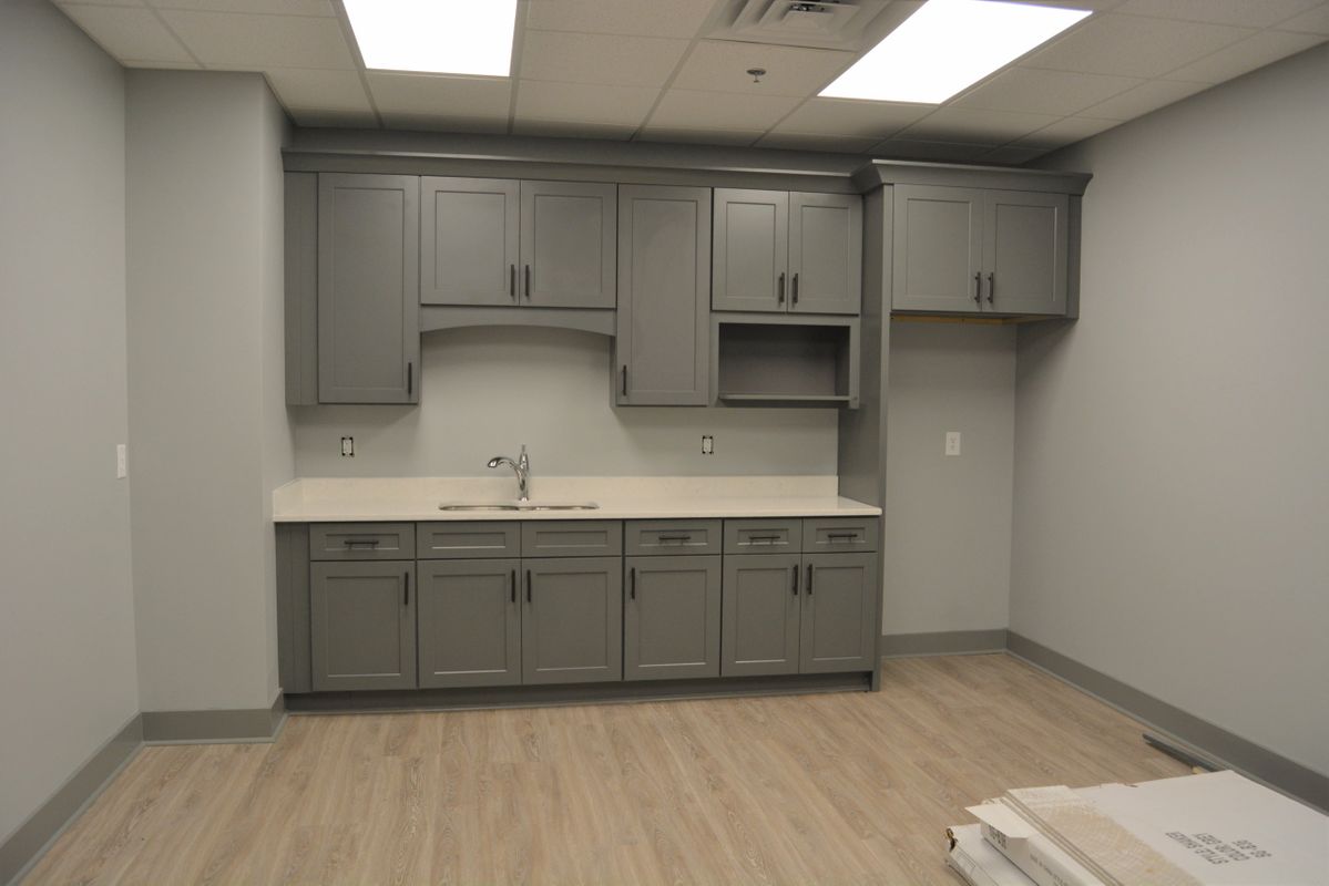 Gray kitchen cabinets in a room with light-colored flooring and white countertops.