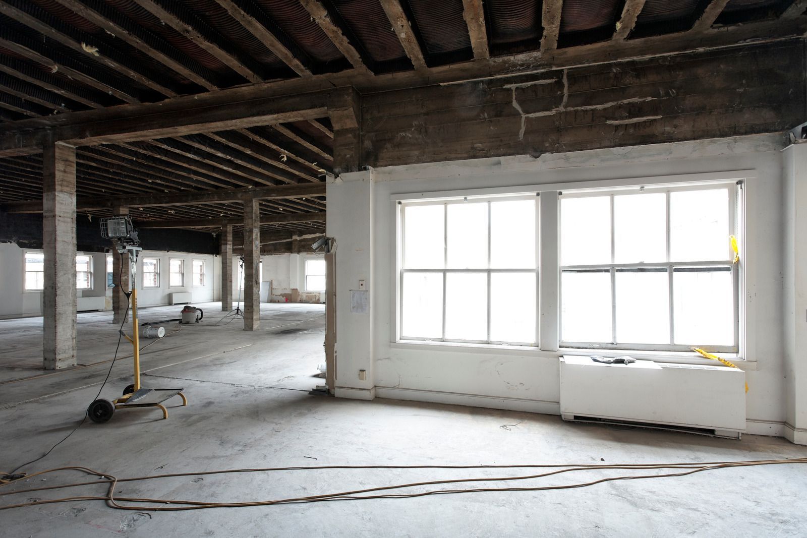 Interior of a building under renovation, with exposed wooden beams, white walls, and a large window.