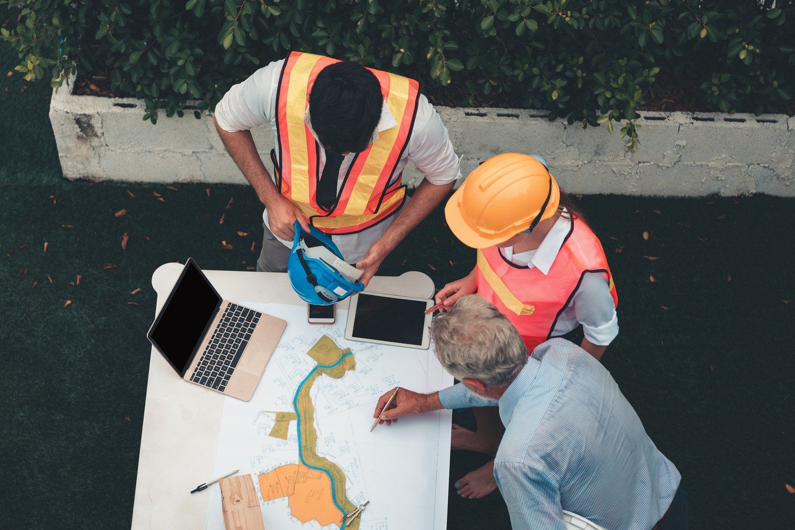 Construction workers in safety vests and helmets reviewing blueprints outdoors.