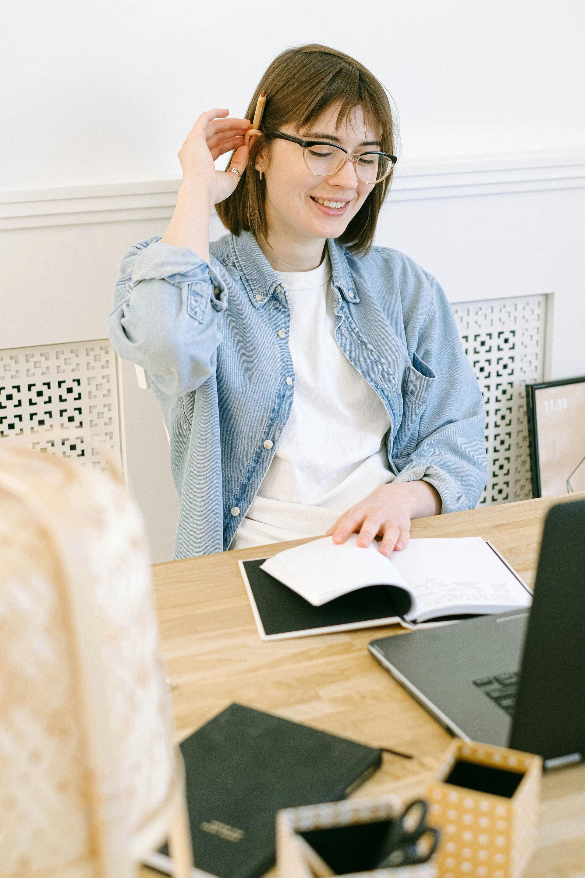 A woman is sitting at a desk with a laptop and a notebook.