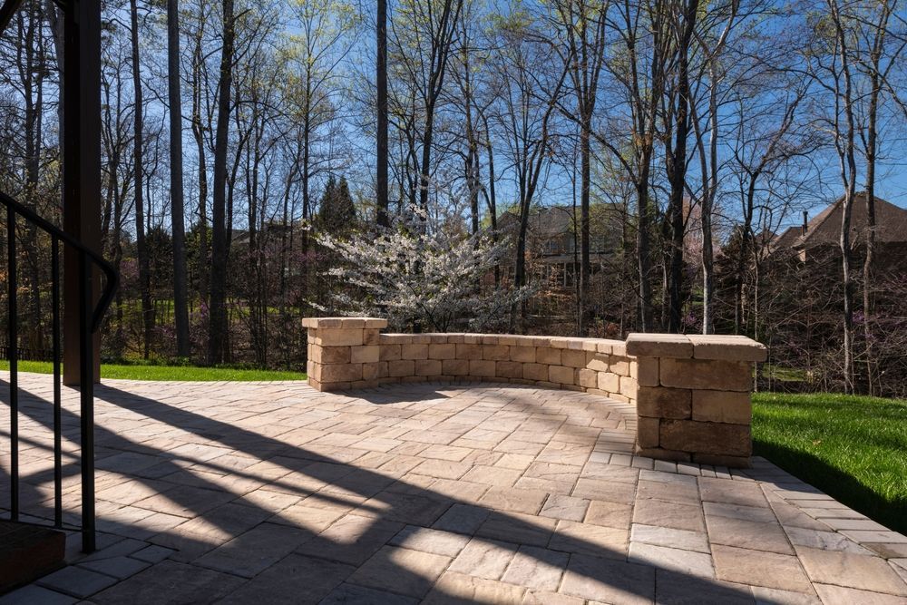 A patio with a stone wall and trees in the background.