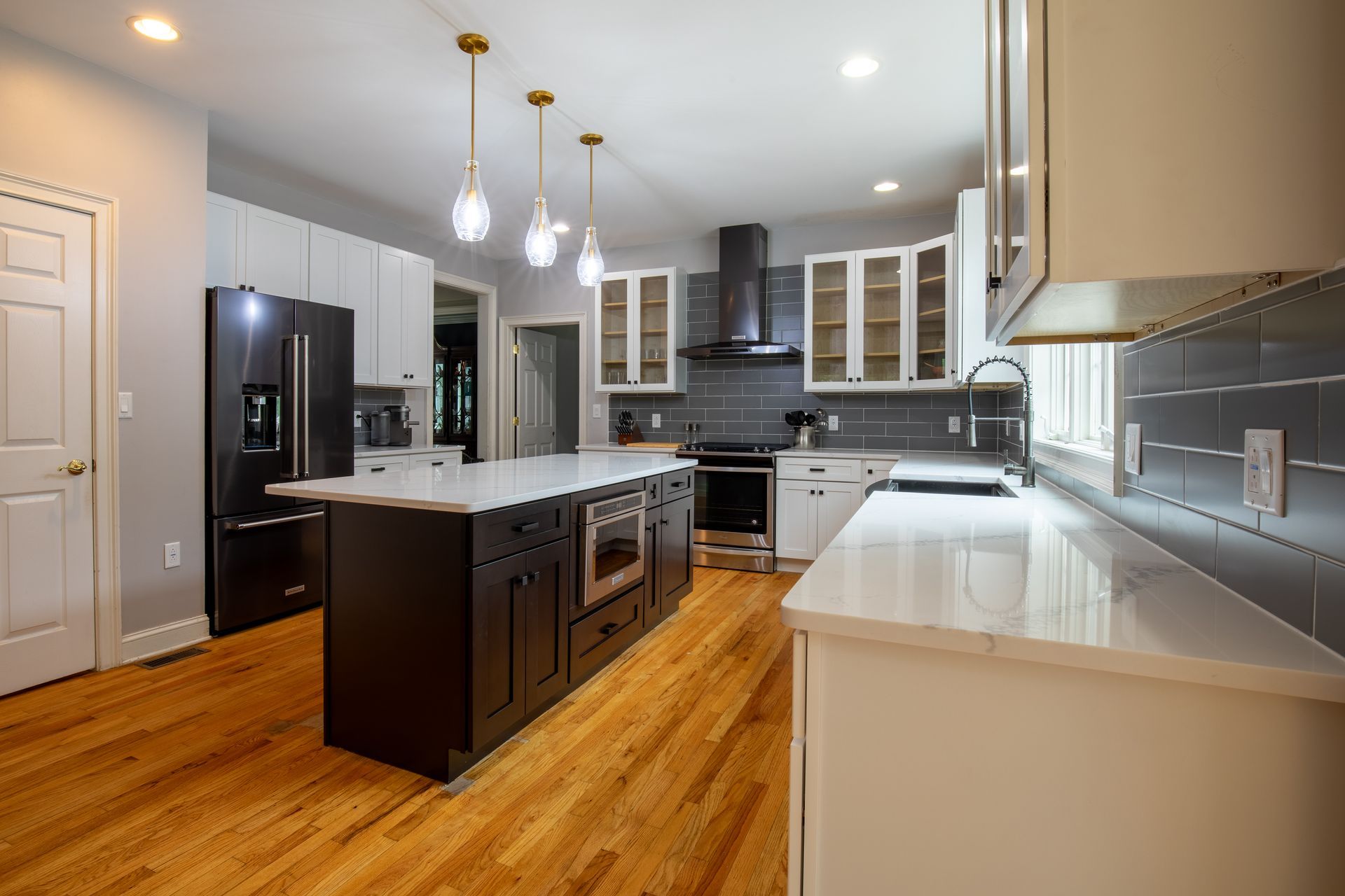 A kitchen with black cabinets , white cabinets , stainless steel appliances , hardwood floors and a large island.