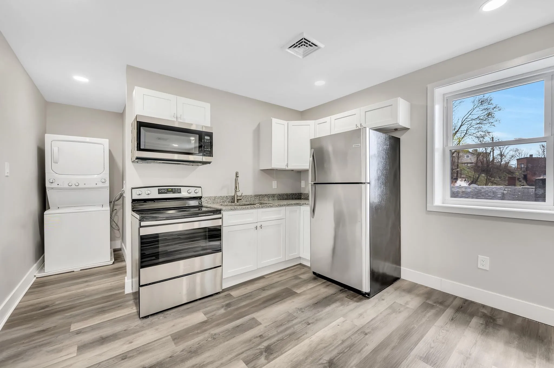 A kitchen with a stove , refrigerator , microwave and a window.