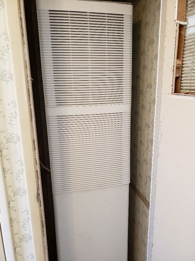 A white air conditioner is sitting in a corner of a room.