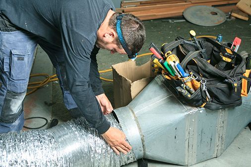 A man is working on a metal pipe next to a tool bag.