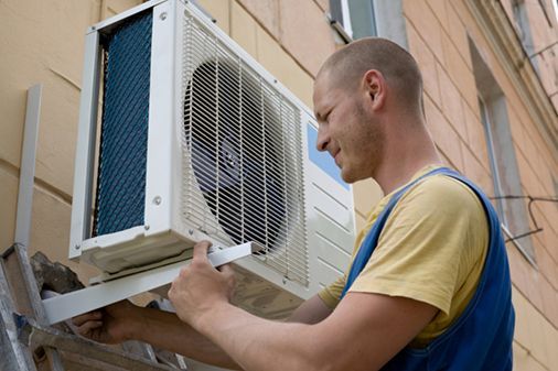 A man is installing an air conditioner on the side of a building.