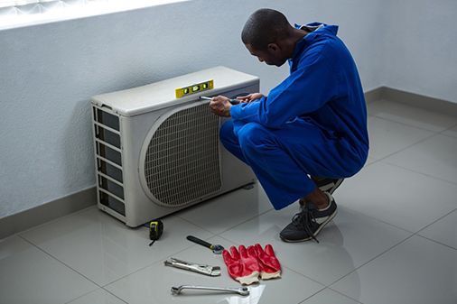A man is kneeling down to fix an air conditioner.