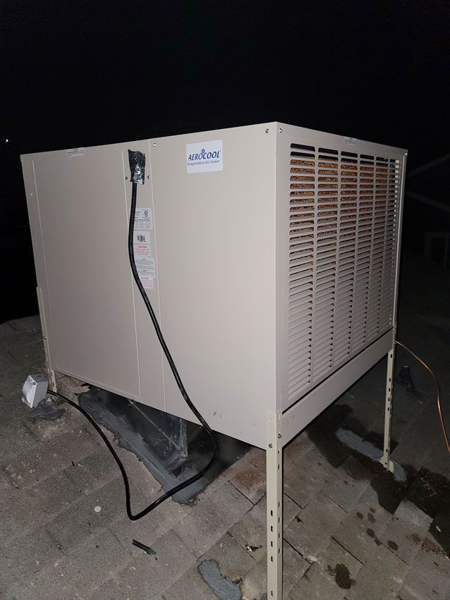A large air conditioner is sitting on top of a brick roof at night.