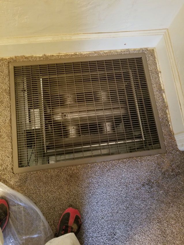 A person is standing next to a heater on the floor in a room.
