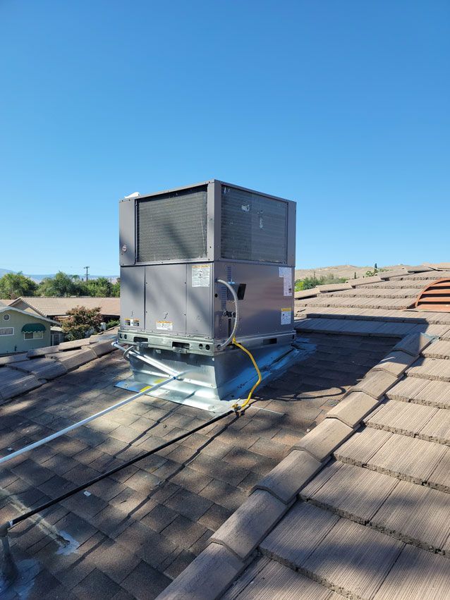 A large air conditioner is sitting on top of a tiled roof.