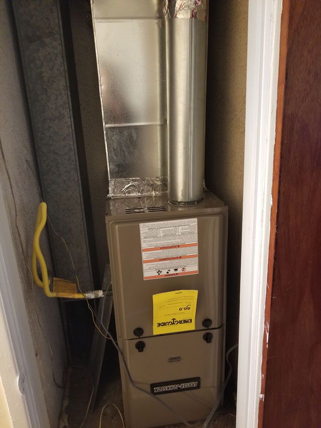A furnace is sitting in a corner of a room next to a door.