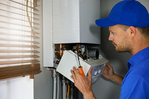 A man is fixing a boiler with a screwdriver.