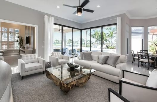 Bright living room with white furniture, large windows overlooking a lake, and a wooden coffee table.