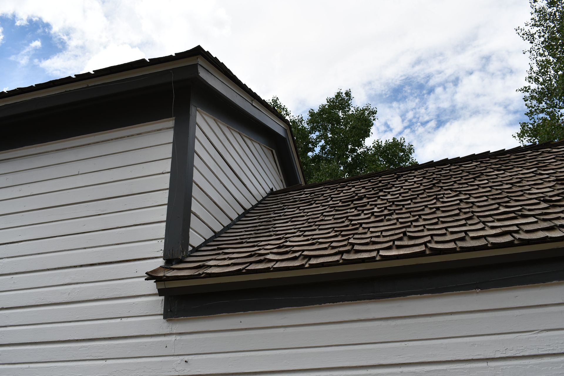 White building with dark trim and shingled roof under a cloudy sky.