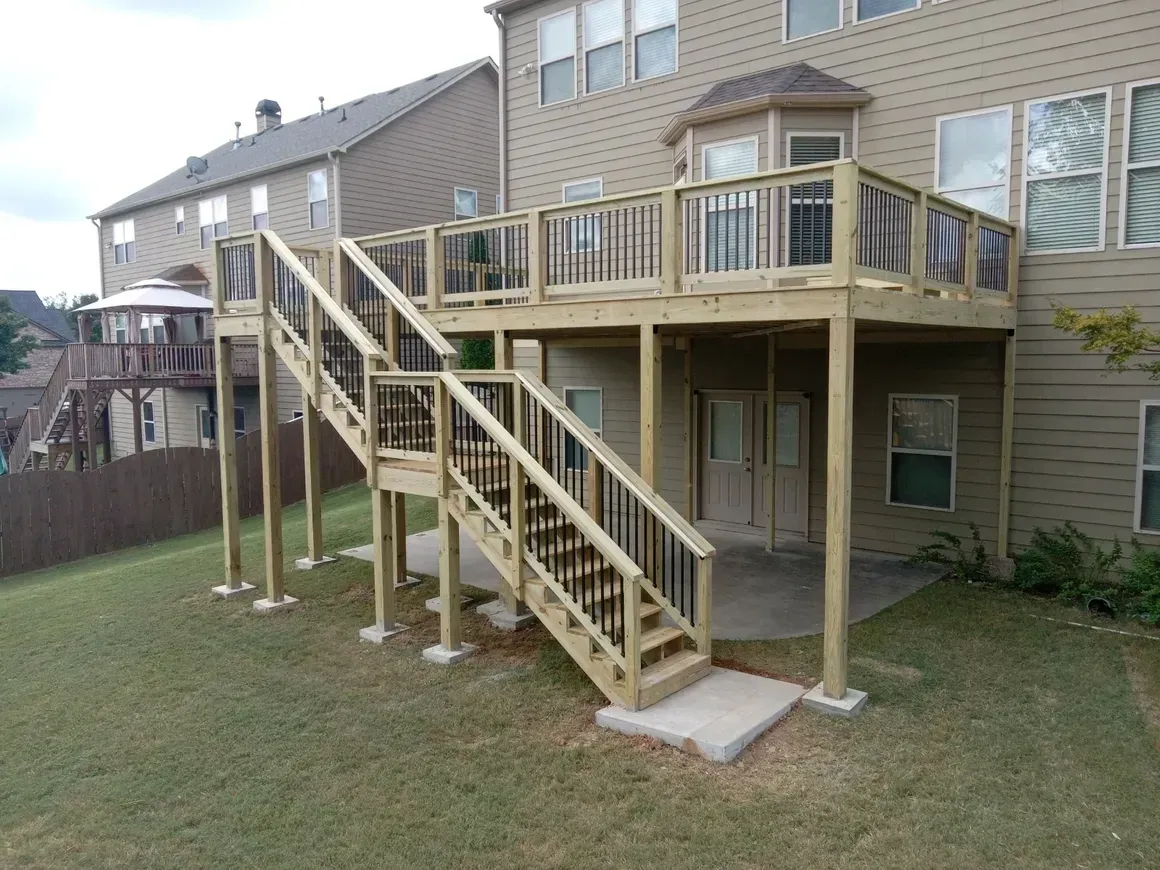 Multi-level wooden deck with stairs and black railings on a grassy backyard.