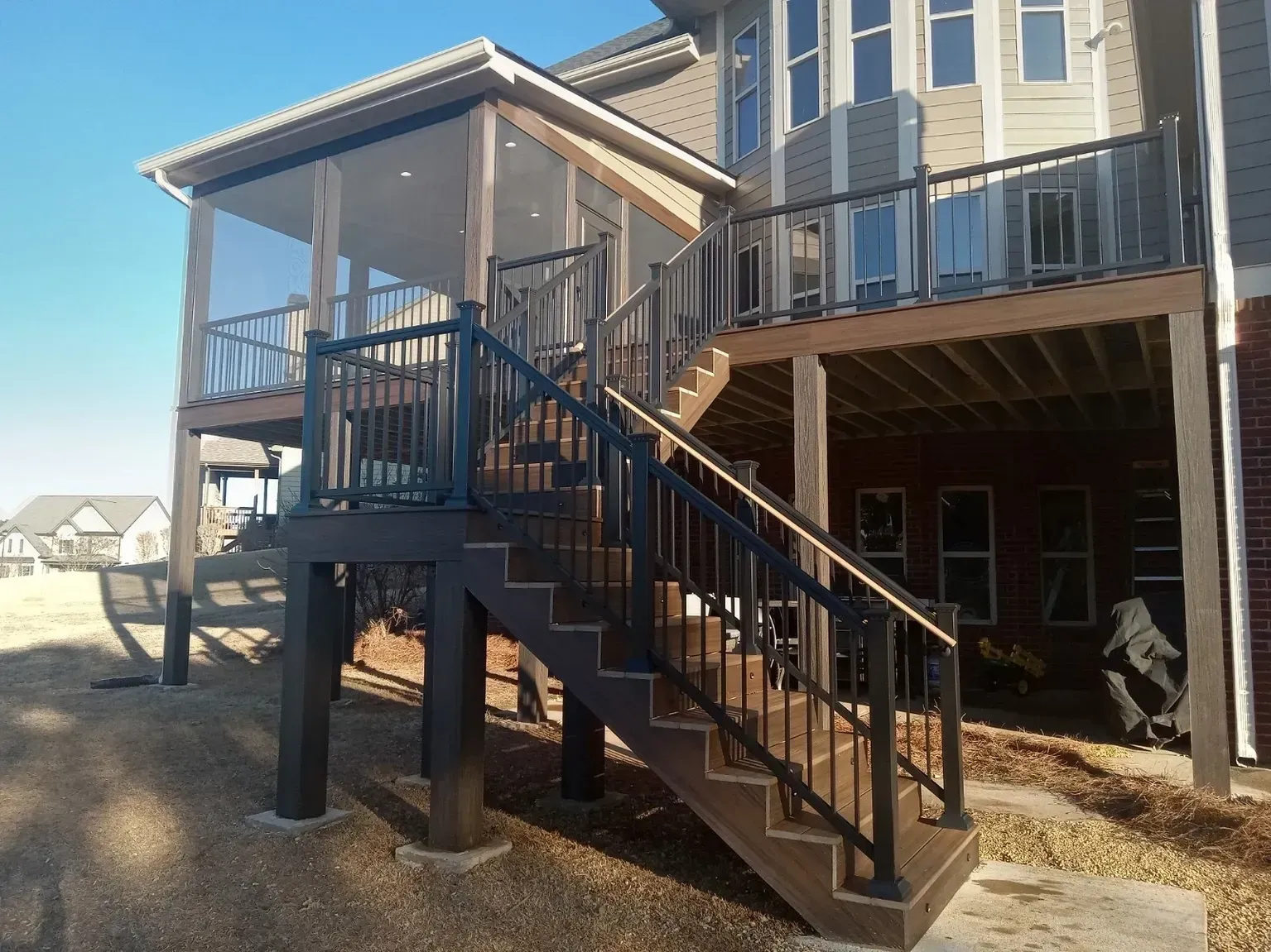 Multi-level deck with stairs and screened-in porch, dark railings and support posts, brown decking, sunny outdoor setting.
