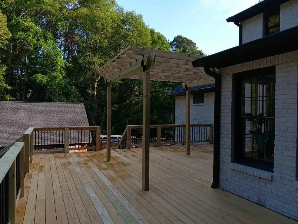 Wooden deck with pergola, attached to a light brick house with dark trim.