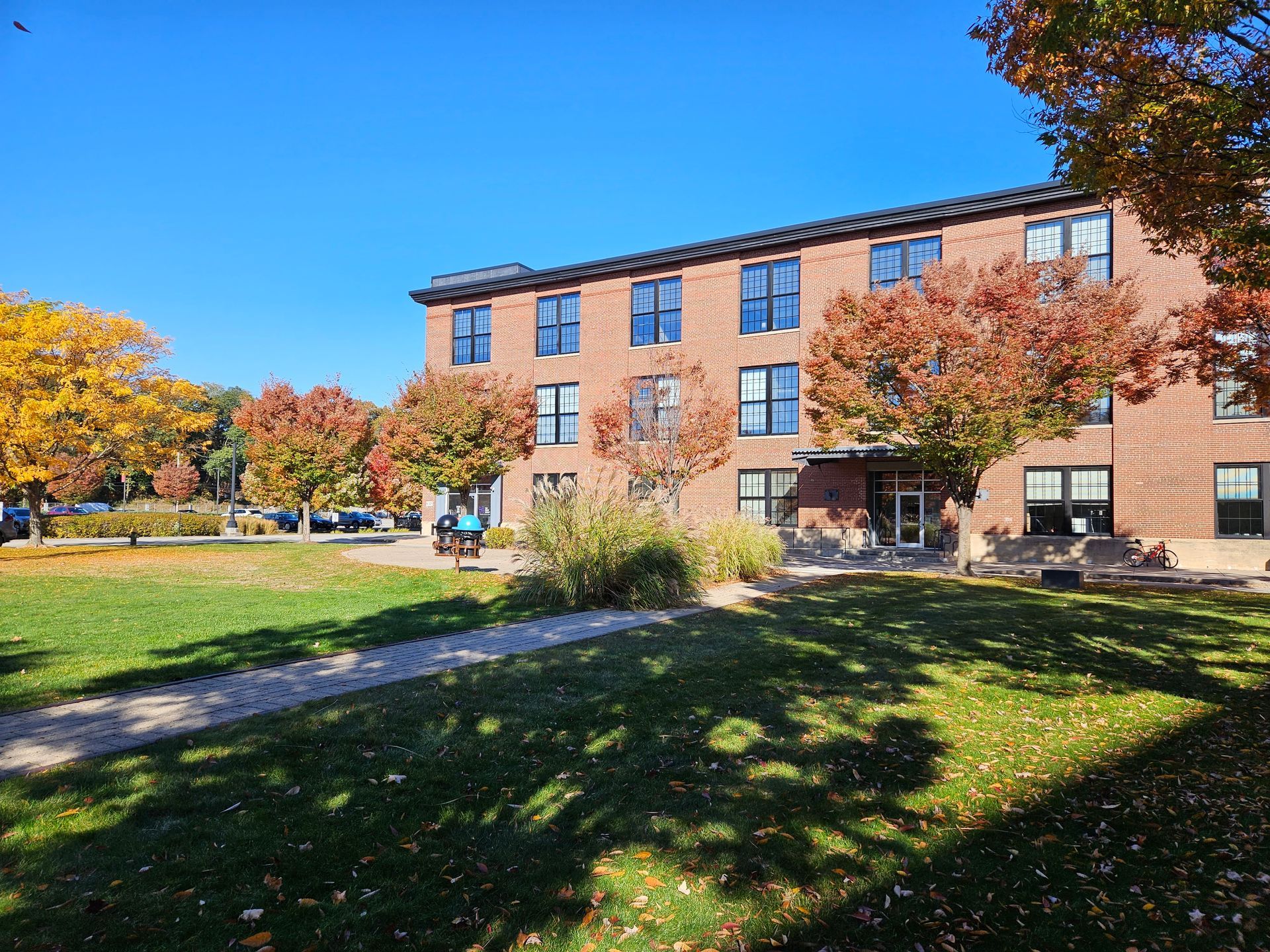 A large brick building with a lot of windows is surrounded by trees and grass.