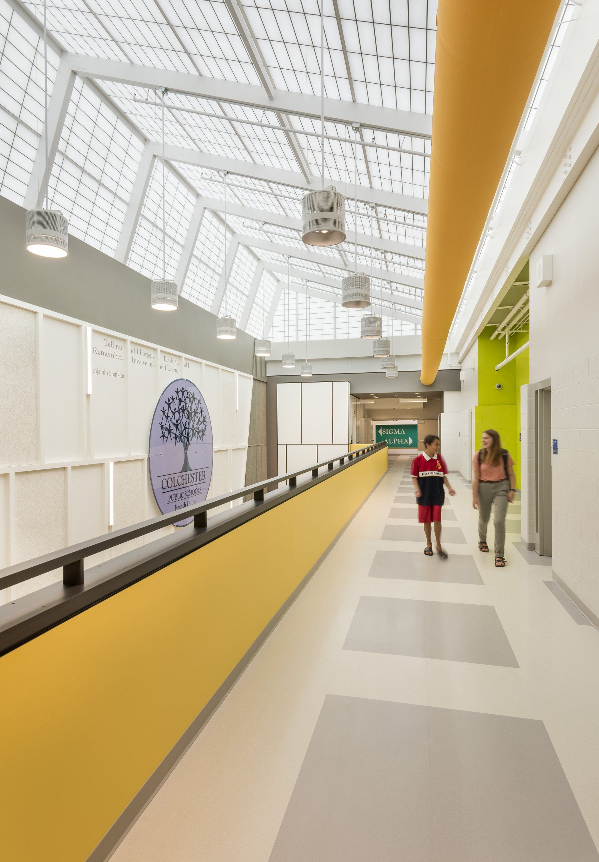 Two people are walking down a long hallway in a building.