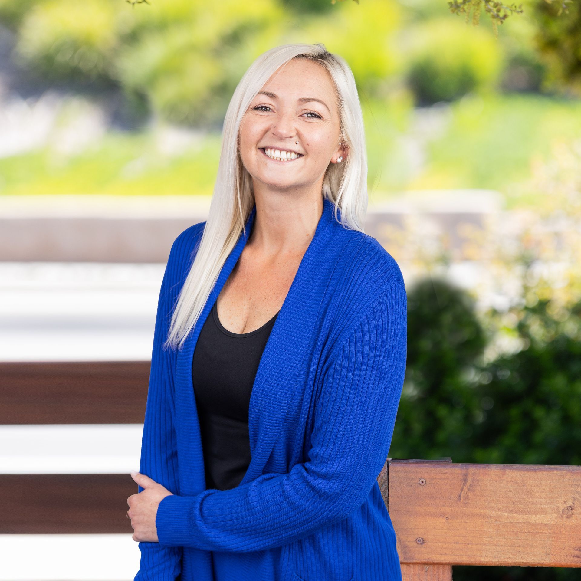Woman with brown hair and a light blue shirt smiles outdoors.