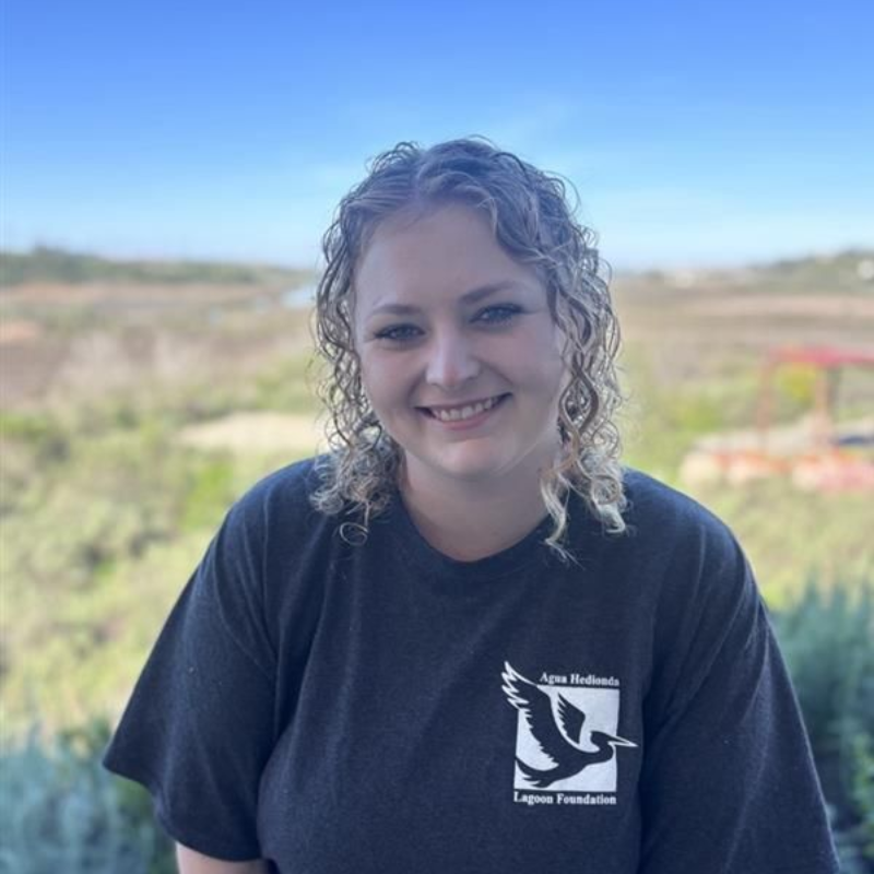 Woman with brown hair and a light blue shirt smiles outdoors.
