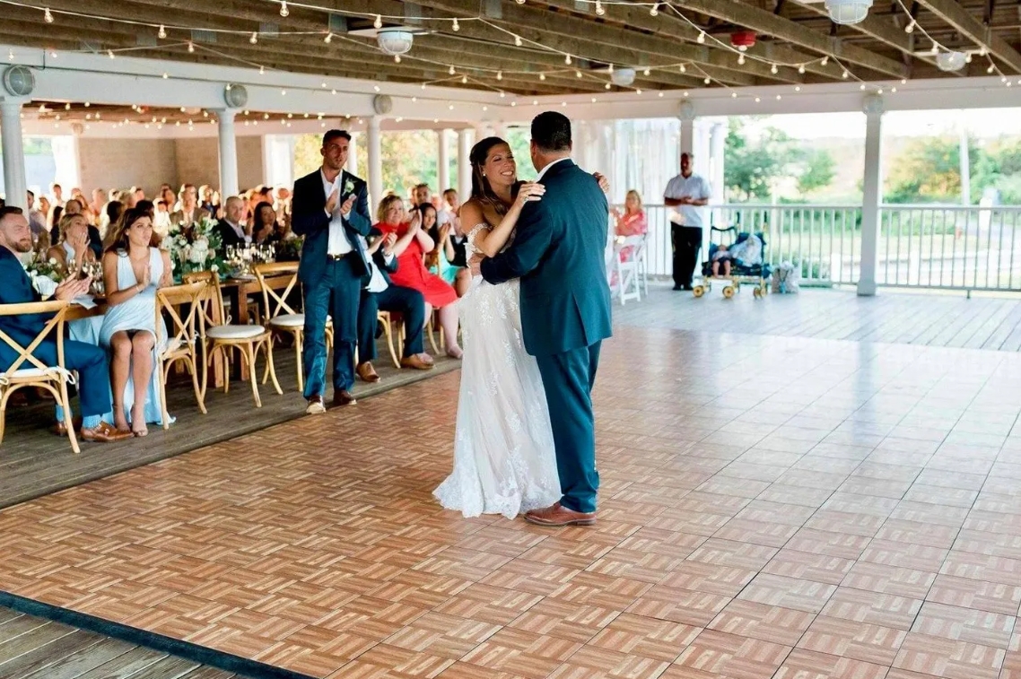 A bride and groom are dancing on a wooden dance floor at their wedding reception.