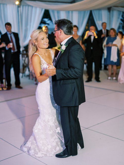 A bride and her father are dancing on a white dance floor.