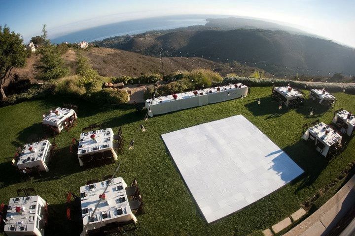 A large white dance floor is in the middle of a lush green field.