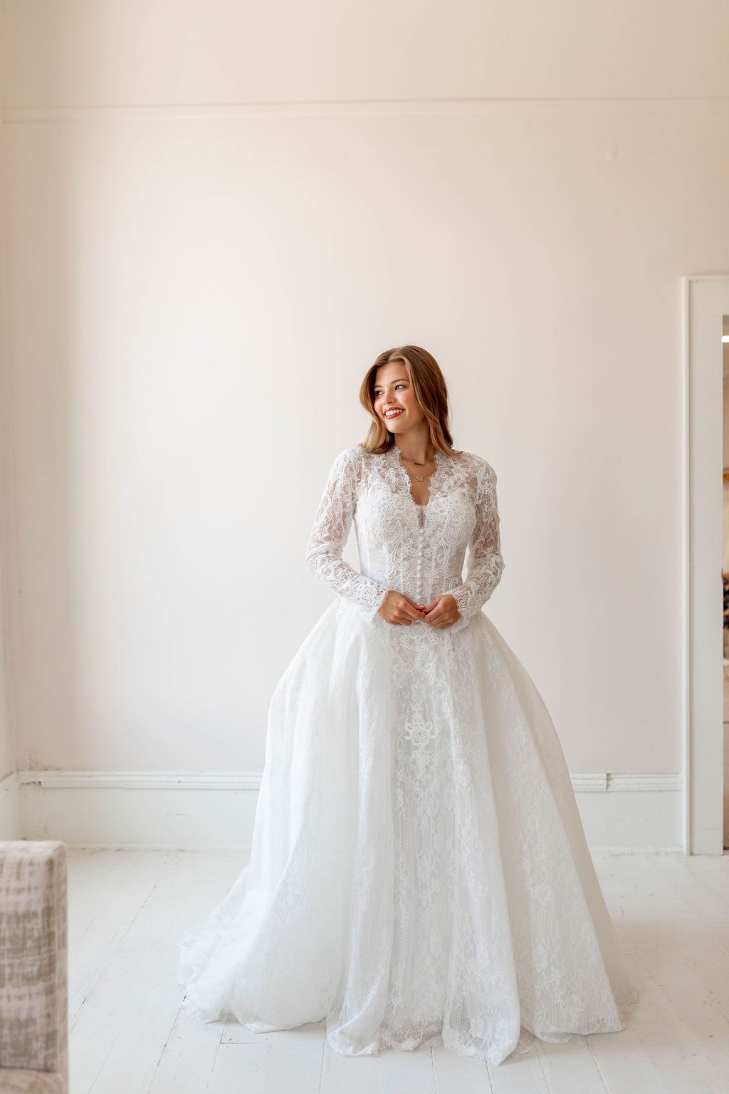 Woman in a white lace wedding gown standing in a bright, minimal room